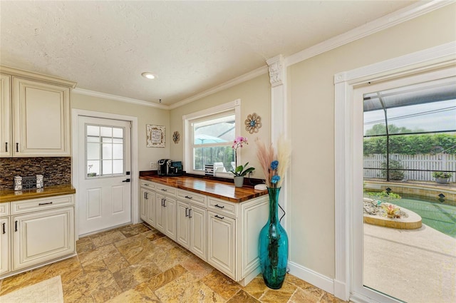 kitchen featuring cream cabinets, wood counters, ornamental molding, and stone tile floors