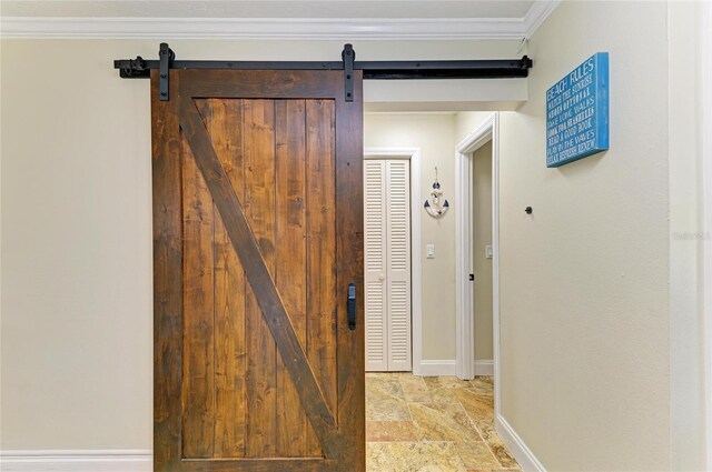 corridor featuring a barn door, stone finish flooring, crown molding, and baseboards