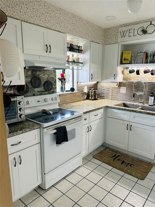 kitchen with under cabinet range hood, a sink, white electric range oven, light tile patterned flooring, and white cabinetry