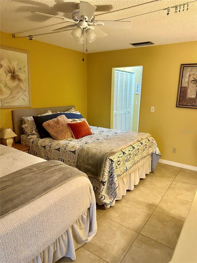 bedroom with a ceiling fan, a textured ceiling, light tile patterned flooring, baseboards, and visible vents