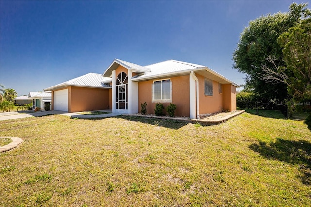 ranch-style home featuring a front lawn, an attached garage, fence, metal roof, and stucco siding