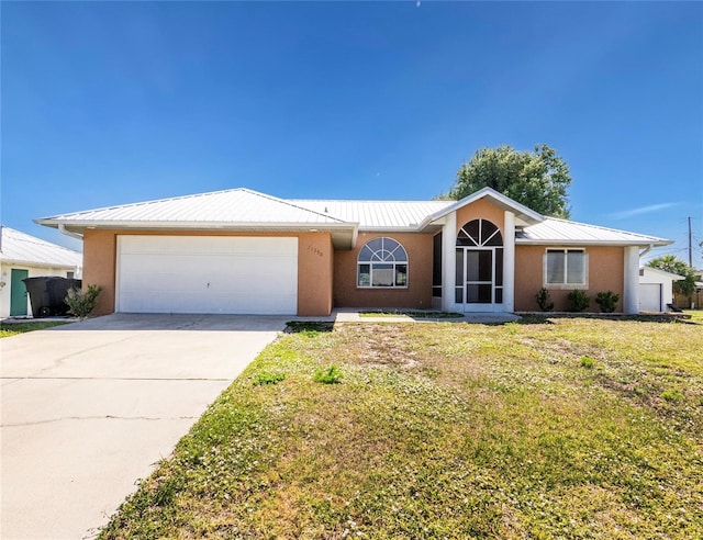 ranch-style home with driveway, metal roof, an attached garage, a front yard, and stucco siding