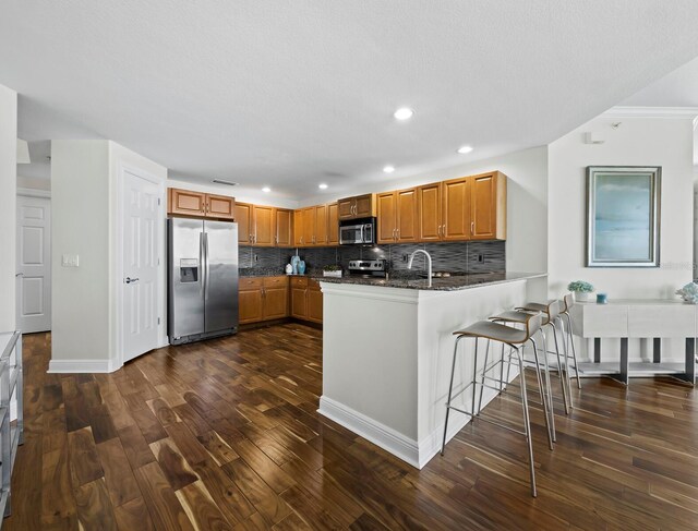 1771 Ringling Blvd Unit 1104, Sarasota, FL 34236 - kitchen featuring brown cabinetry, decorative backsplash, a peninsula, dark wood finished floors, and stainless steel appliances