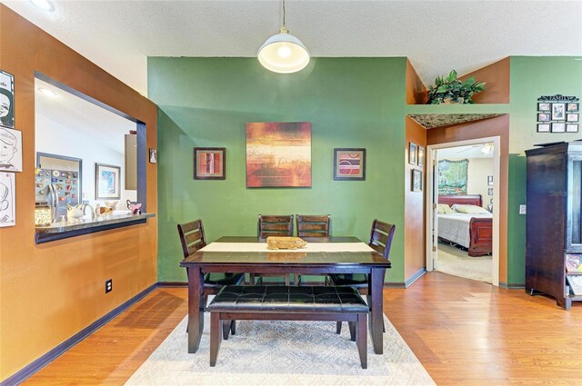 dining room featuring wood finished floors, vaulted ceiling, a textured ceiling, and baseboards