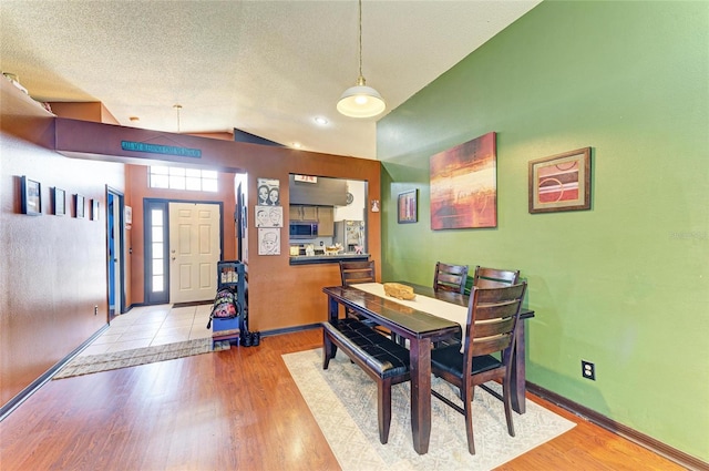 dining space featuring light wood-style floors, a textured ceiling, and baseboards