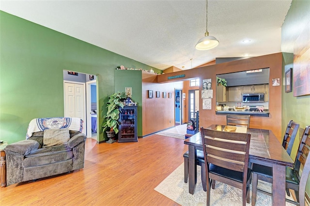 dining area with light wood-type flooring, lofted ceiling, beverage cooler, and a textured ceiling