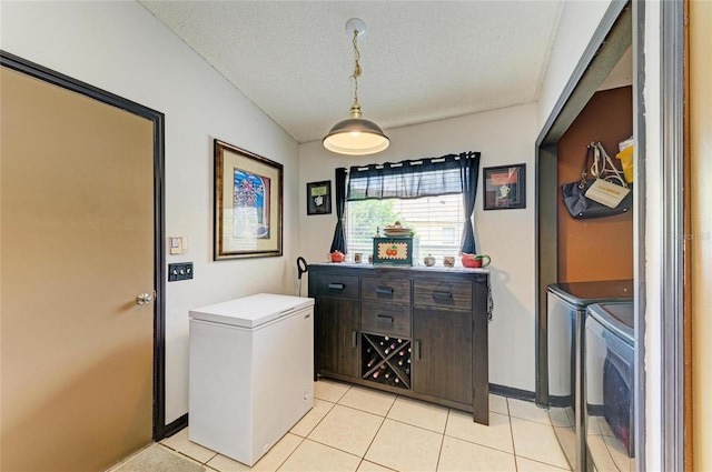 clothes washing area with washing machine and dryer, light tile patterned floors, a textured ceiling, and baseboards