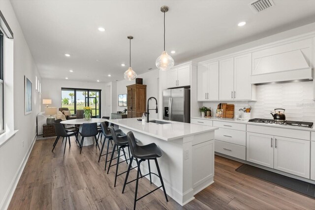 kitchen featuring appliances with stainless steel finishes, a sink, custom exhaust hood, recessed lighting, and open floor plan