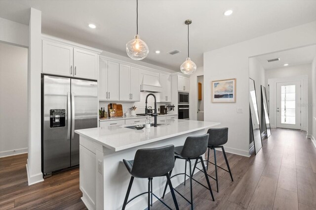 kitchen featuring appliances with stainless steel finishes, a kitchen island with sink, white cabinetry, light countertops, and dark wood-style flooring