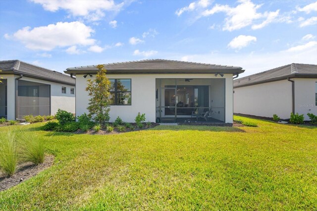 back of house with a sunroom, a lawn, stucco siding, and a tile roof