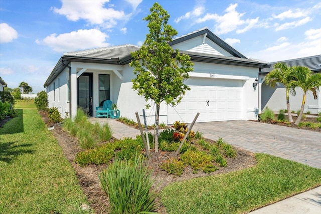 view of side of home featuring decorative driveway, a garage, stucco siding, and a lawn