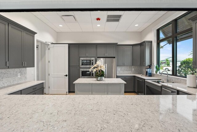 kitchen with appliances with stainless steel finishes, a sink, a drop ceiling, decorative backsplash, and light stone countertops