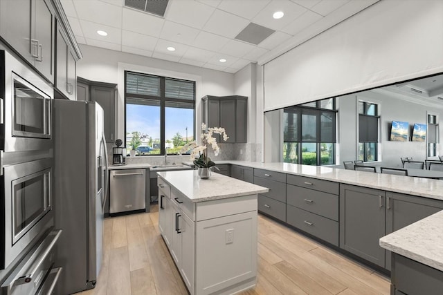 kitchen with appliances with stainless steel finishes, gray cabinets, a center island, light stone countertops, and backsplash