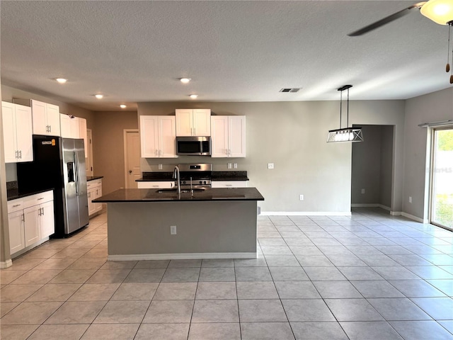 kitchen featuring dark countertops, an island with sink, white cabinetry, a sink, and stainless steel appliances