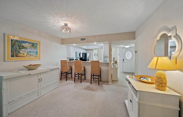 kitchen featuring visible vents, light carpet, a kitchen breakfast bar, white cabinetry, and stainless steel appliances