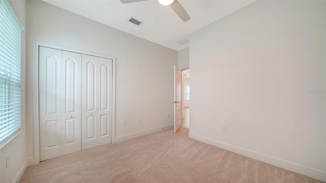 unfurnished bedroom featuring light colored carpet, a closet, baseboards, and a ceiling fan