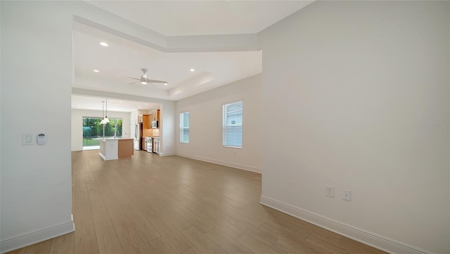 unfurnished living room featuring ceiling fan, baseboards, wood finished floors, a tray ceiling, and recessed lighting