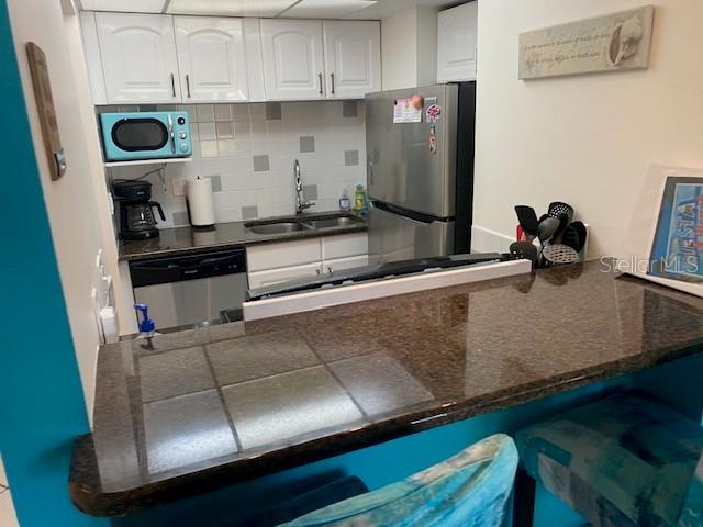 6157 E Midnight Pass Rd Unit B51, Sarasota, FL 34242 - kitchen with stainless steel appliances, a sink, white cabinetry, decorative backsplash, and a kitchen bar