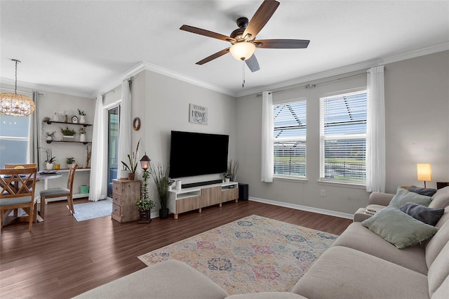 living area featuring ceiling fan with notable chandelier, baseboards, dark wood-type flooring, and crown molding