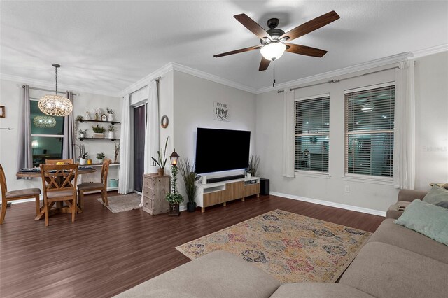 living area with ceiling fan with notable chandelier, baseboards, dark wood-type flooring, and ornamental molding