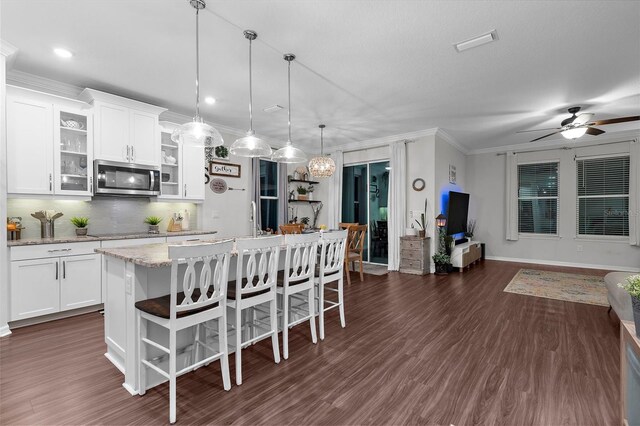 kitchen with stainless steel microwave, dark wood-style flooring, black electric stovetop, a breakfast bar, and a kitchen island