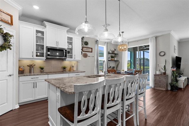 kitchen featuring dark wood-style floors, a sink, stainless steel microwave, ornamental molding, and a breakfast bar area