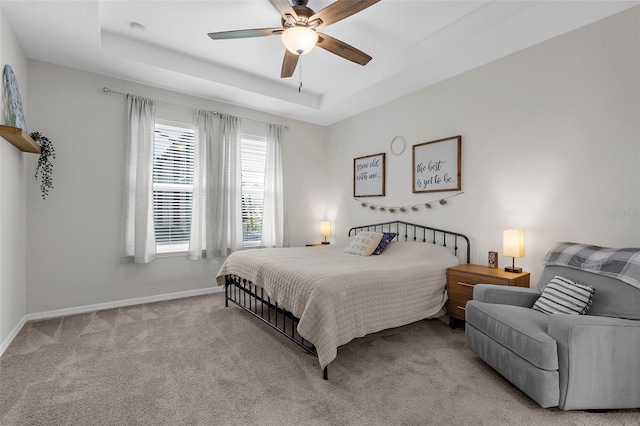 carpeted bedroom with a ceiling fan, baseboards, and a tray ceiling