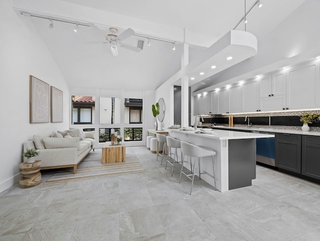 kitchen with rail lighting, high vaulted ceiling, a kitchen breakfast bar, light countertops, and ceiling fan