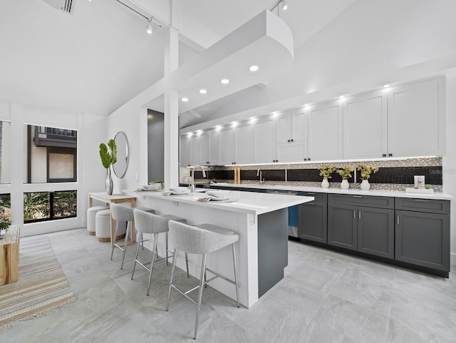 kitchen featuring gray cabinets, track lighting, light countertops, a breakfast bar area, and high vaulted ceiling