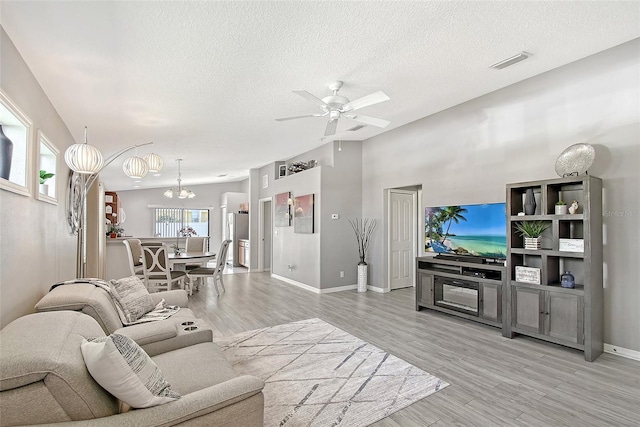 living room with light wood-style flooring, a textured ceiling, baseboards, visible vents, and ceiling fan with notable chandelier