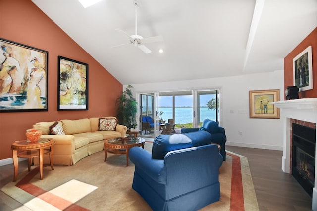 living room with ceiling fan, a brick fireplace, wood finished floors, high vaulted ceiling, and a water view