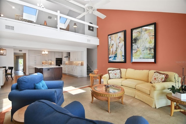 living room featuring visible vents, stairway, high vaulted ceiling, light wood-type flooring, and a ceiling fan