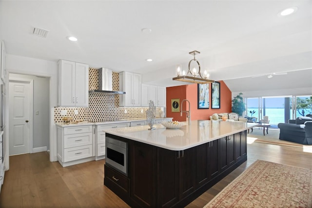 kitchen featuring light countertops, stainless steel microwave, wall chimney exhaust hood, and white cabinetry