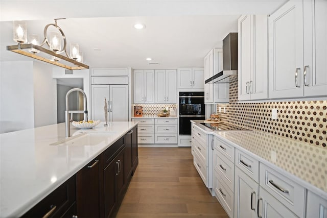 kitchen featuring a sink, light countertops, wall chimney range hood, and black appliances