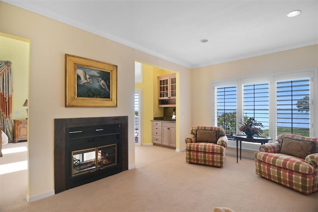 living area featuring ornamental molding, a glass covered fireplace, light carpet, baseboards, and recessed lighting