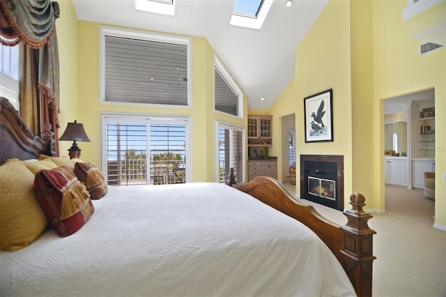 carpeted bedroom with a skylight, high vaulted ceiling, a glass covered fireplace, and visible vents