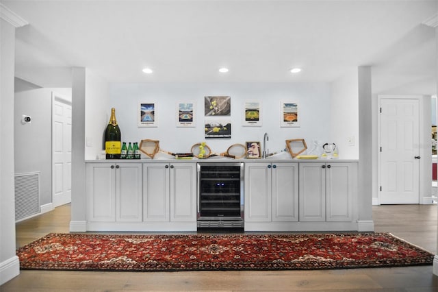 bar with visible vents, wood finished floors, beverage cooler, indoor wet bar, and a sink
