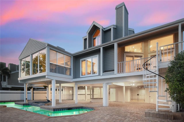 back of house at dusk featuring a chimney, an outdoor pool, a patio area, stairway, and fence