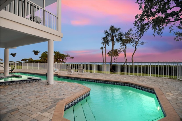 pool at dusk featuring a fenced backyard, a patio, a water view, and a pool with connected hot tub