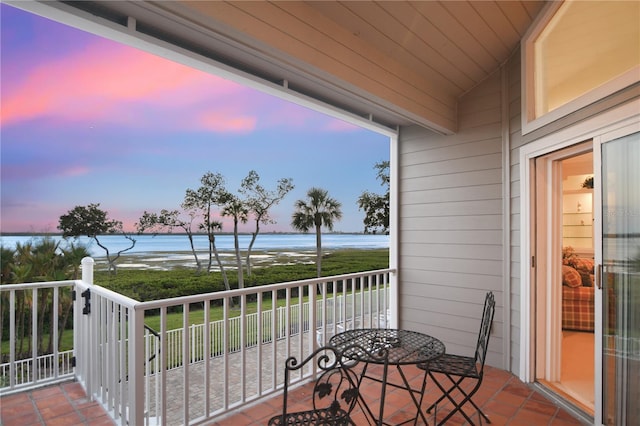 balcony at dusk featuring a water view