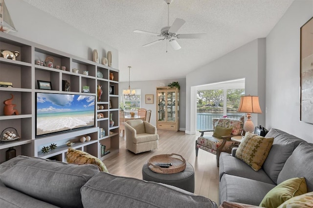 living room featuring vaulted ceiling, wood finished floors, a textured ceiling, and ceiling fan with notable chandelier