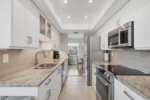 kitchen with white cabinets, stainless steel appliances, a sink, crown molding, and a raised ceiling