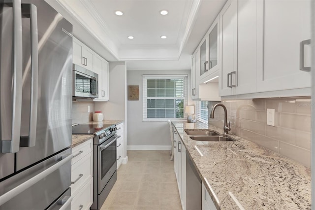 kitchen featuring a sink, a raised ceiling, white cabinets, backsplash, and appliances with stainless steel finishes
