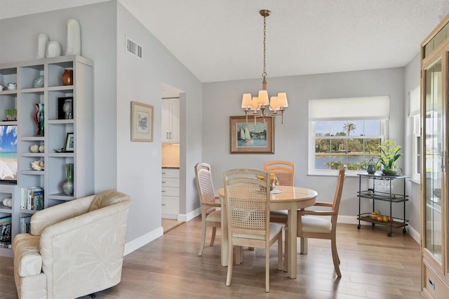 dining room featuring vaulted ceiling, light wood-type flooring, an inviting chandelier, baseboards, and visible vents