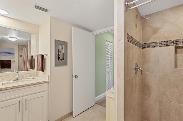 bathroom with baseboards, visible vents, vanity, and tiled shower