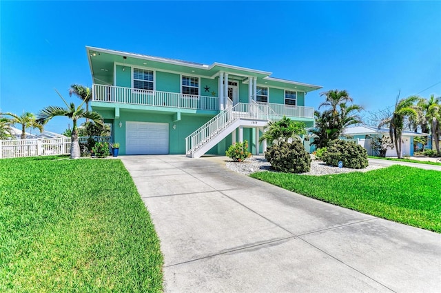 beach home with a porch, driveway, a front yard, an attached garage, and stairs