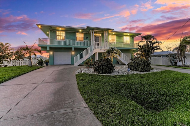 coastal inspired home with a garage, a front lawn, covered porch, stairs, and concrete driveway