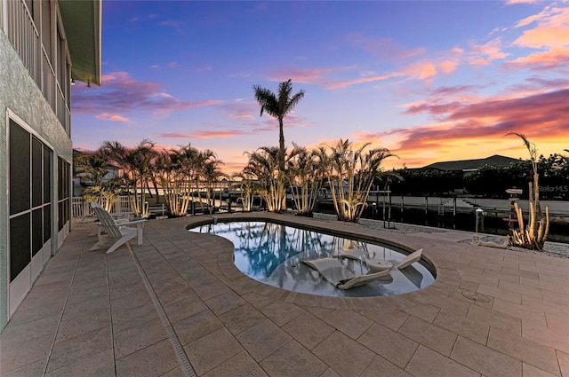 pool at dusk with a patio, a dock, and an outdoor pool