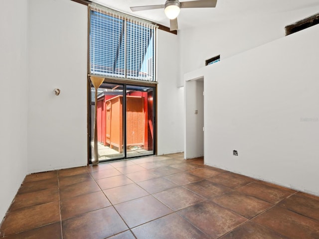 tiled spare room with a ceiling fan, a towering ceiling, and floor to ceiling windows