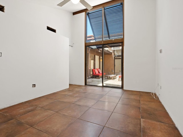 empty room featuring high vaulted ceiling, a ceiling fan, tile patterned floors, and a wall of windows